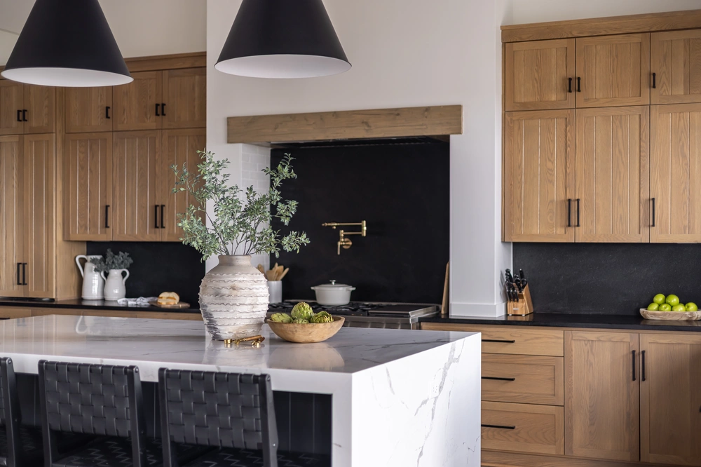 Beautifully remodeled kitchen in Incline Village, featuring warm wooden cabinets, a sleek black backsplash, modern pendant lighting, and a spacious marble island with bar seating.