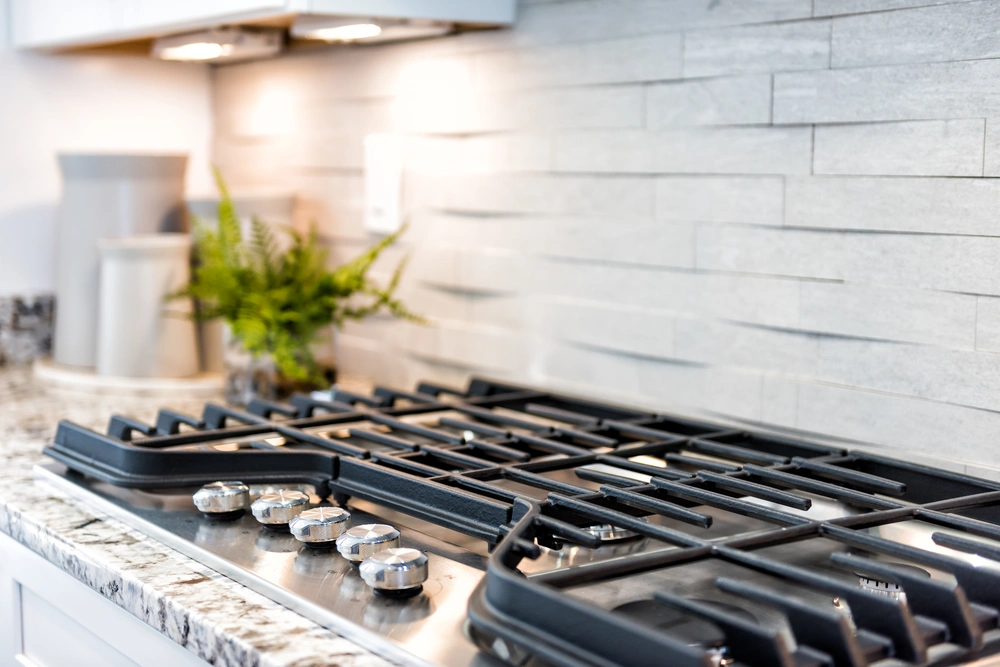 Close-up of a sleek gas cooktop installed during a kitchen remodel in Incline Village, highlighted by a textured white tile wall.