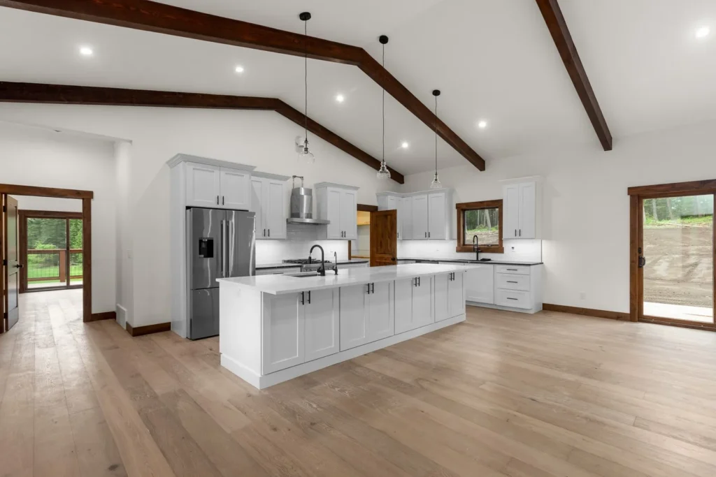 Spacious modern kitchen renovation in Minden with white cabinets, wood beams, and natural light from large windows.