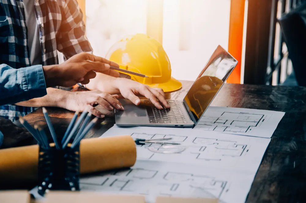 Contractor reviewing blueprints and project roadmap on a laptop during pre-construction planning