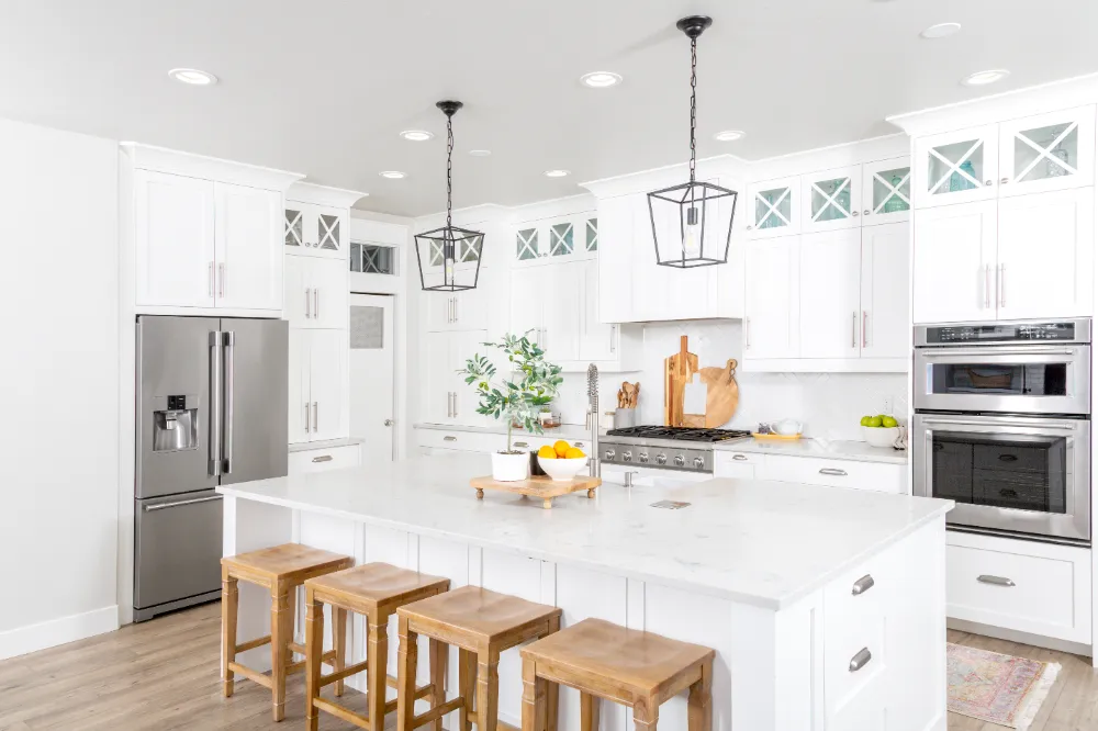 Bright modern kitchen remodel in Carson City featuring white cabinetry, large island with wooden stools, pendant lighting, and stainless-steel appliances.